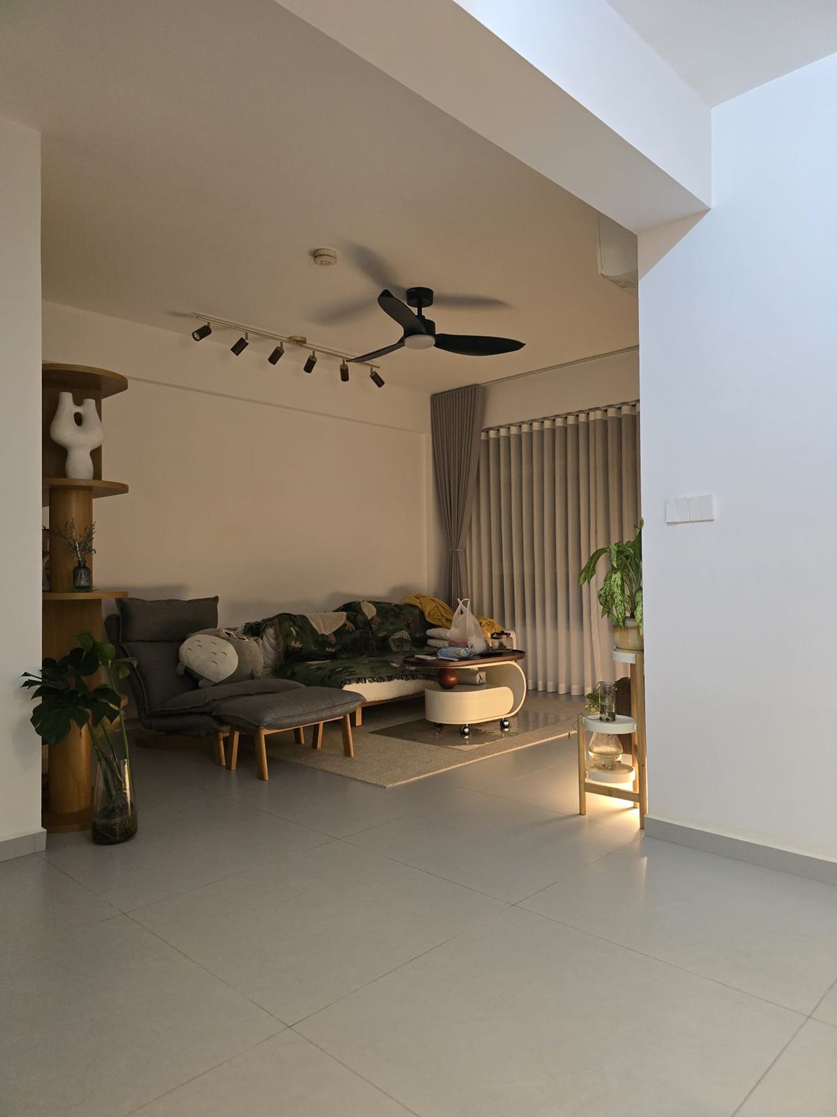 Living room with a grey sofa, a ceiling fan and track lights, a curved timber shelf and sheer curtains along the window wall.