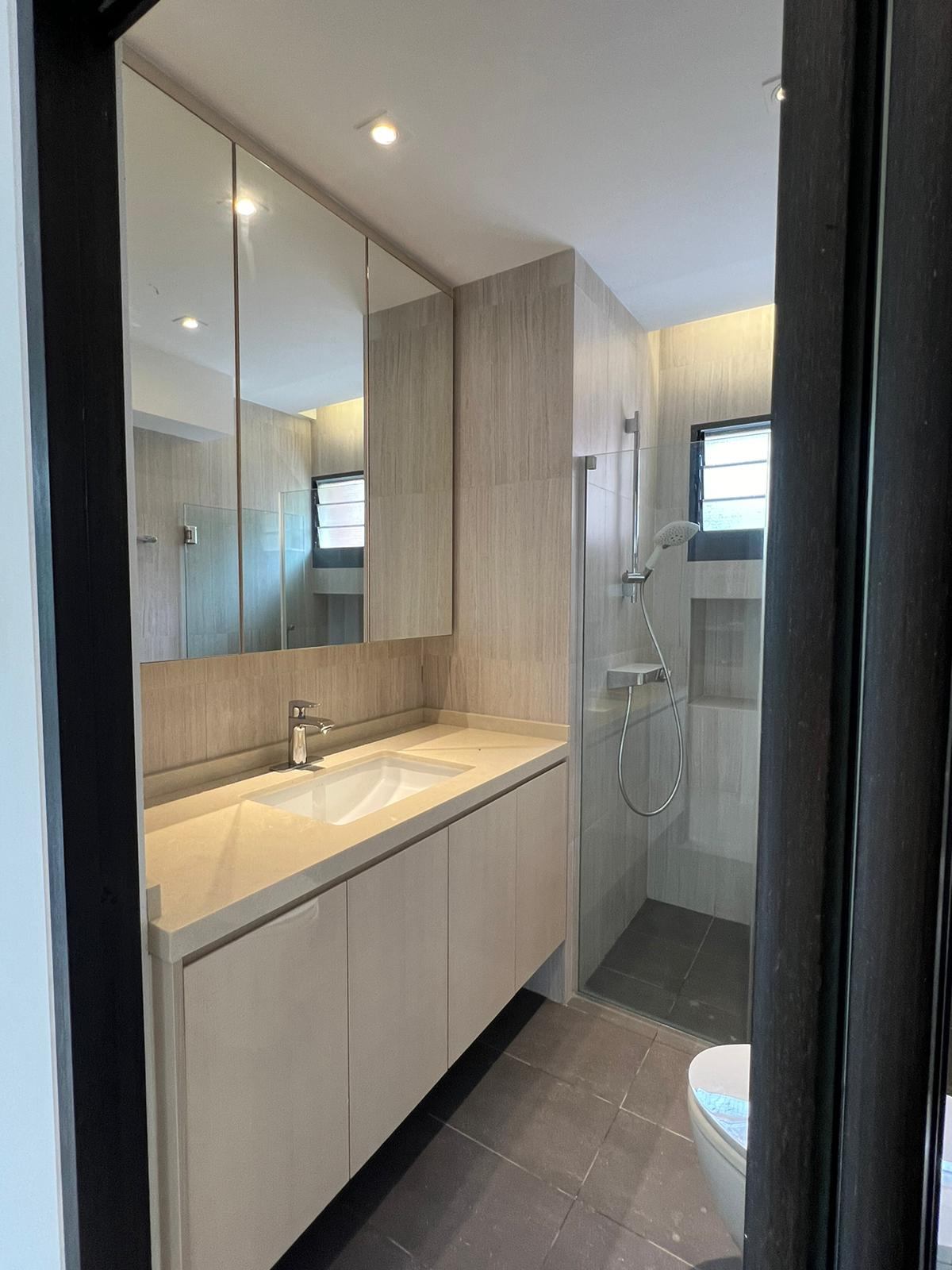 A bathroom vanity with a mirrored cabinet and warm under-cabinet lighting, beside a glass shower.