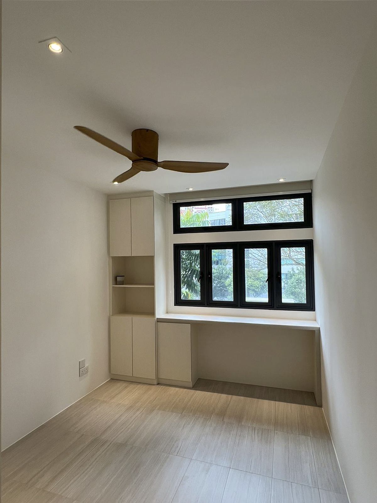 A bedroom with a ceiling fan, a built-in desk and shelving beside the window.