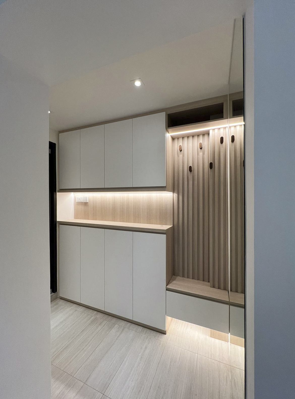 The storage wall at the entry, with white cabinets, an open lit shelf and the fluted panel.