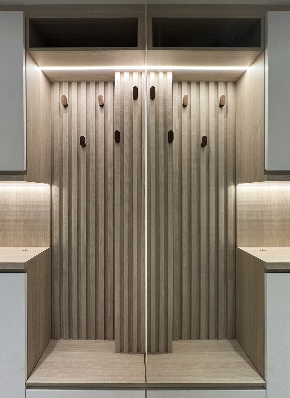 A fluted timber panel with round hooks above a bench, lit from above and below.