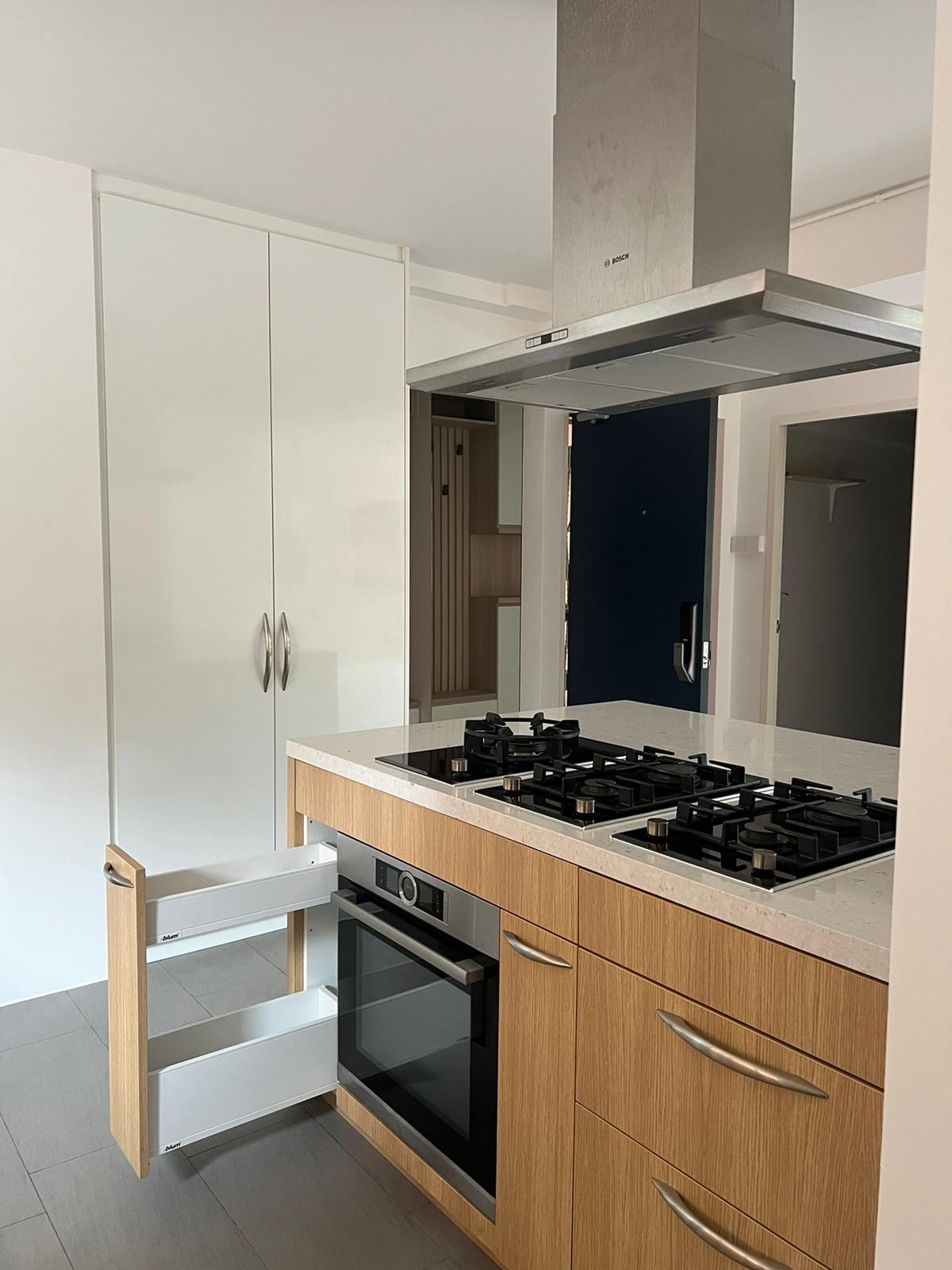The island hob and oven below a stainless hood, with a pull-out storage unit.