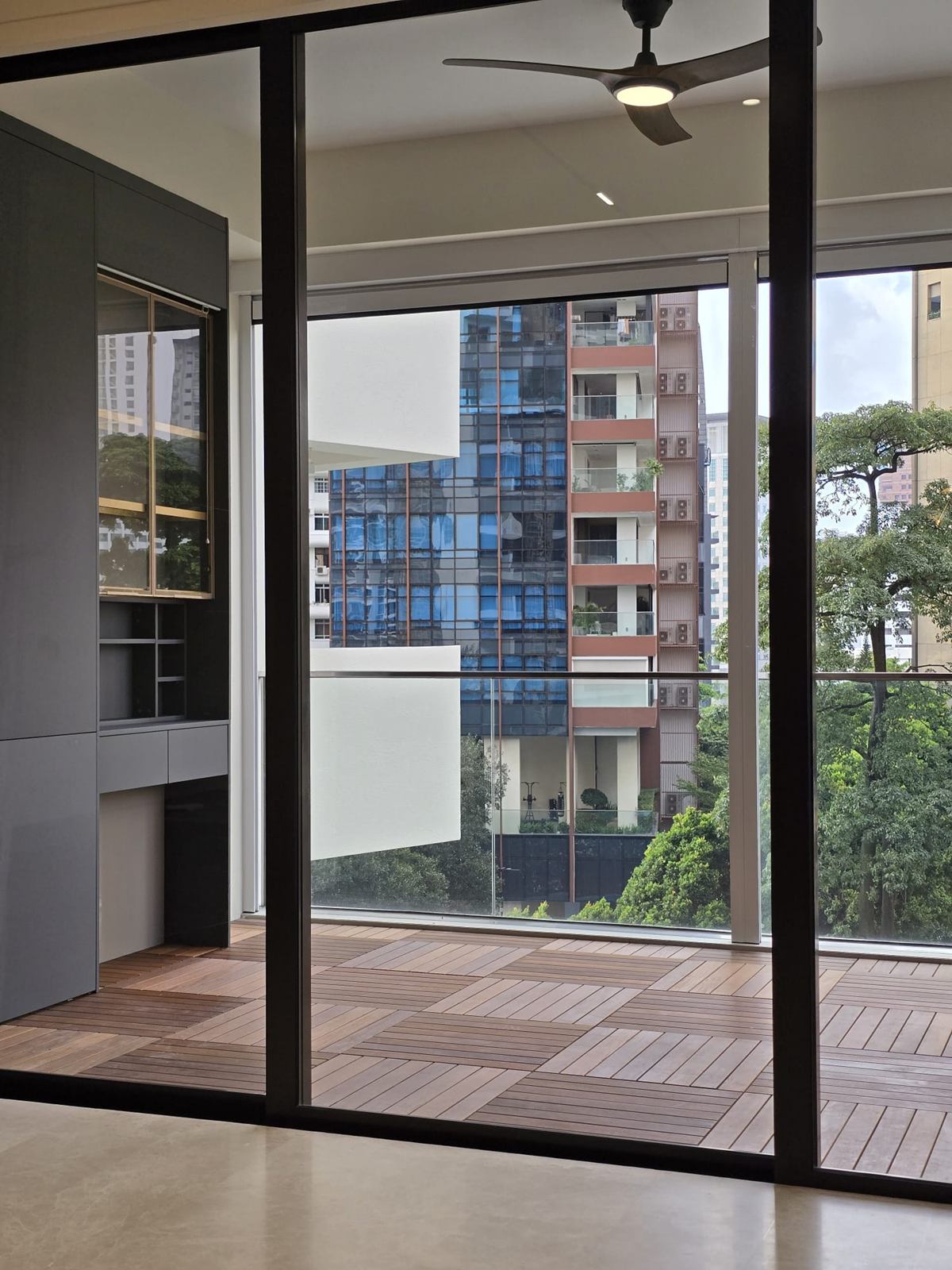 Floor-to-ceiling glazing opening onto a timber-decked balcony, with a ceiling fan and dark joinery to the left.