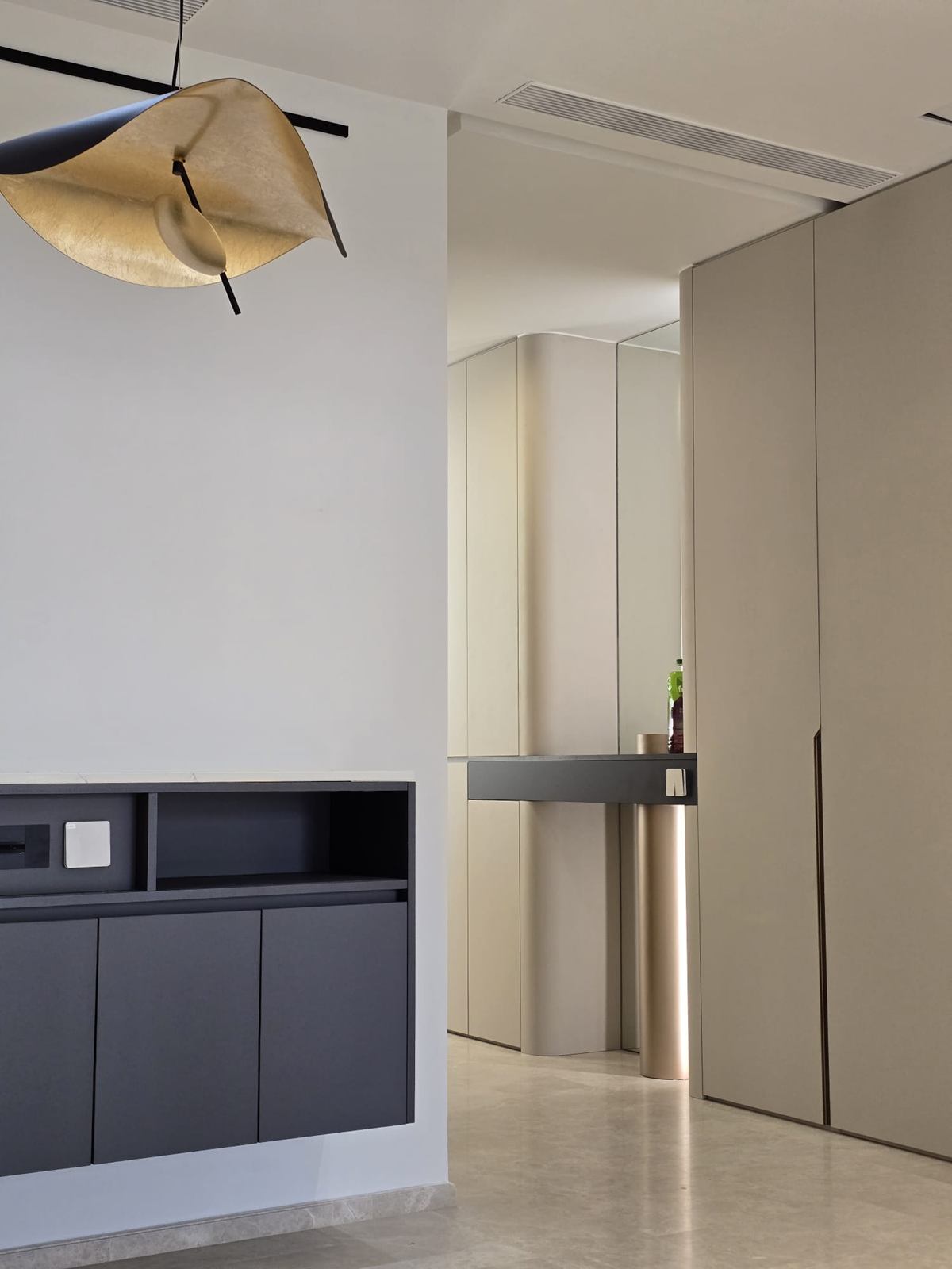 A folded gold-leaf pendant over a dark wall cabinet, with curved pale joinery and a slim console beyond.